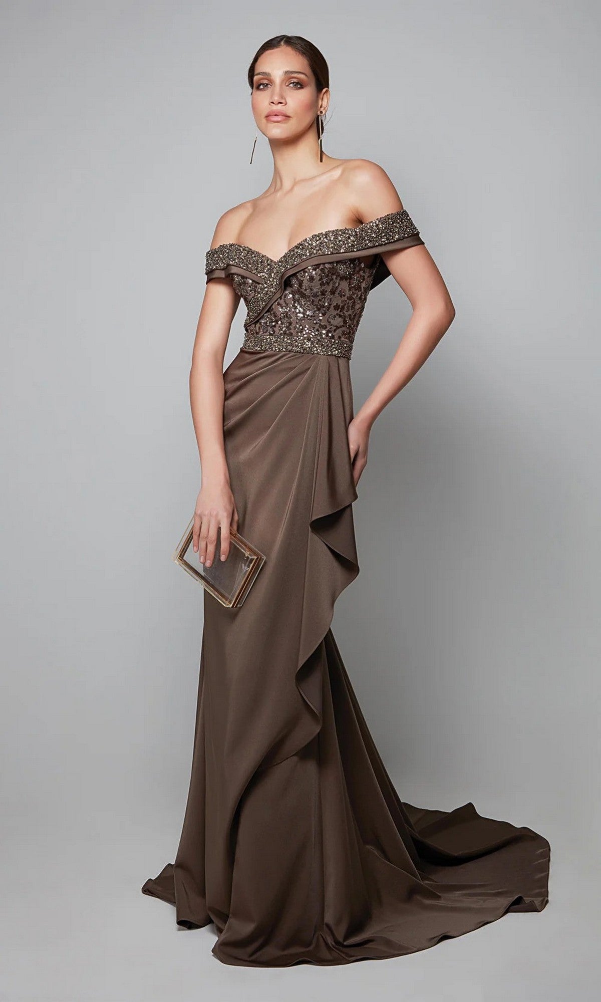 A woman poses against a plain gray background in the Alyce 27619, a floor-length brown off-the-shoulder formal dress with a beaded bodice and small clutch—ideal as an elegant mother-of-the-bride gown.